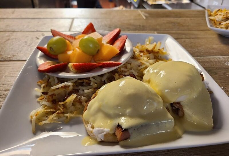 eggs benedict and hash browns plate with fruit on the side